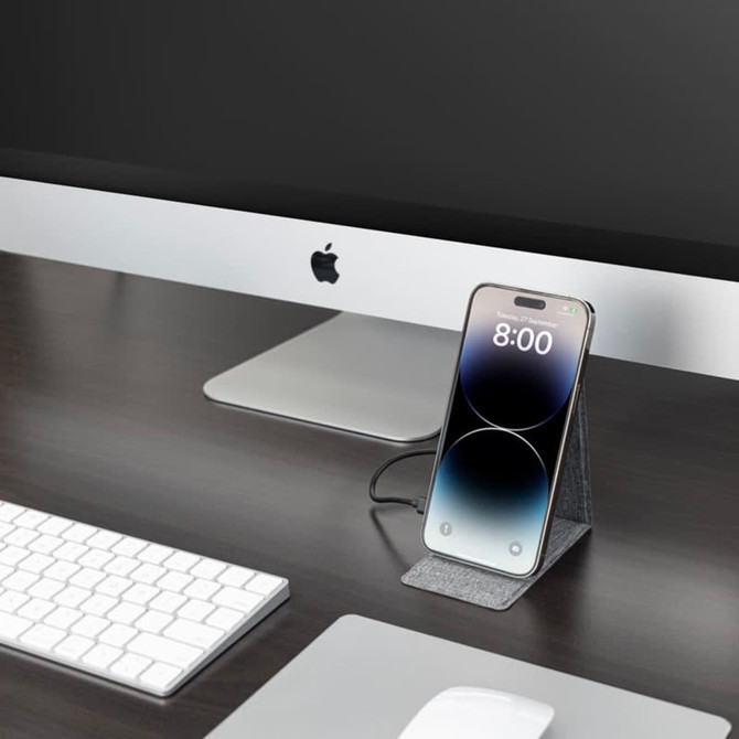 A wireless charger in dark grey, holding a smartphone, placed on a desk beside a computer and keyboard. A wireless charger in dark grey, holding a smartphone, placed on a desk beside a computer and keyboard.