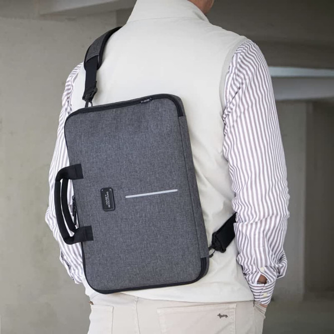 A grey laptop case with a handle and shoulder strap, worn by a person in a light vest and striped shirt.