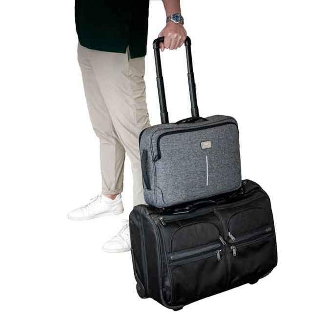 A grey laptop bag with wheels is stacked on a black wheeled suitcase, held by a person in casual attire. A grey laptop bag with wheels is stacked on a black wheeled suitcase, held by a person in casual attire.