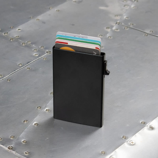 A black RFID case holding multiple cards, set against a metallic surface. The case features a clip on the side.