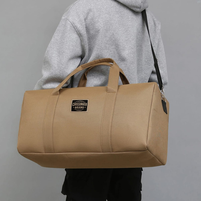 A durable duffle bag in tan, featuring sturdy handles and a shoulder strap, with a logo on the front.