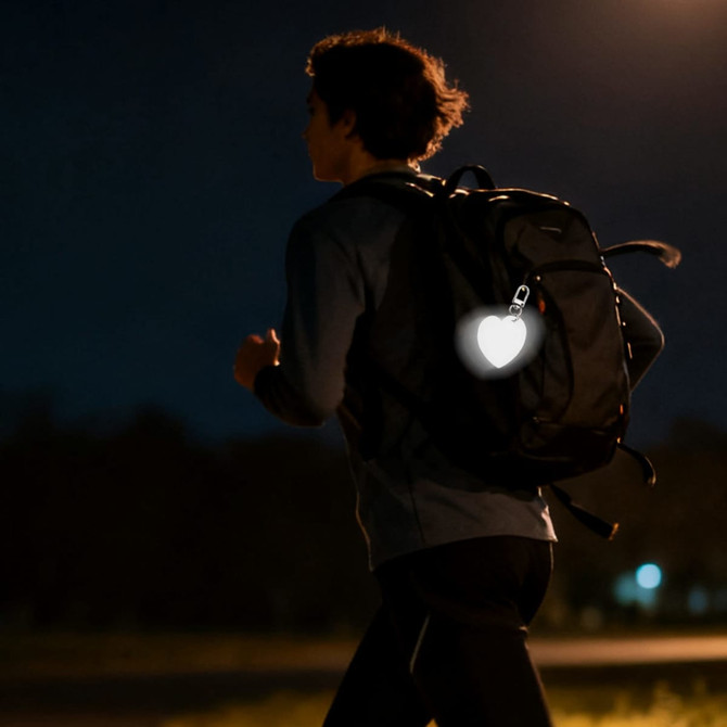 A reflective heart-shaped keychain attached to a backpack, glowing in the dark, with a person walking in the background.