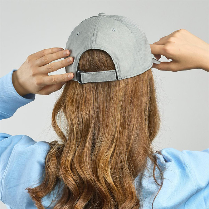 A grey cap with an adjustable strap, seen from the back, worn by a person with wavy hair.