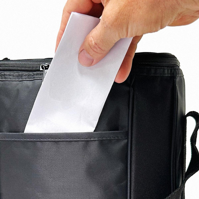 A drink bottle cooler in black with a hand placing a letter into its front pocket. It features a zipper and side handle.