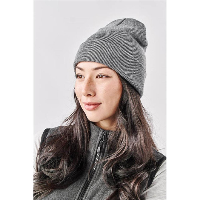 A grey knit beanie worn by a woman with long hair, featuring a subtle logo on the side.