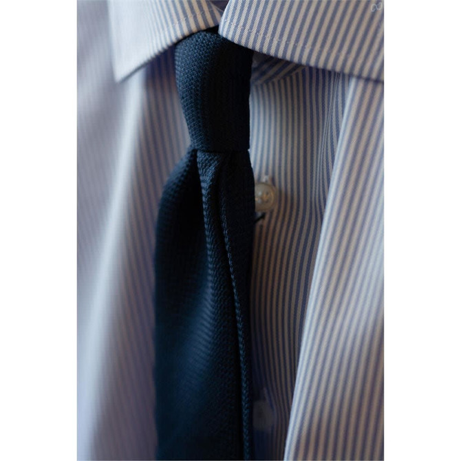 A button-up shirt with light blue and white stripes featuring a solid black tie. It has a logo on the collar.