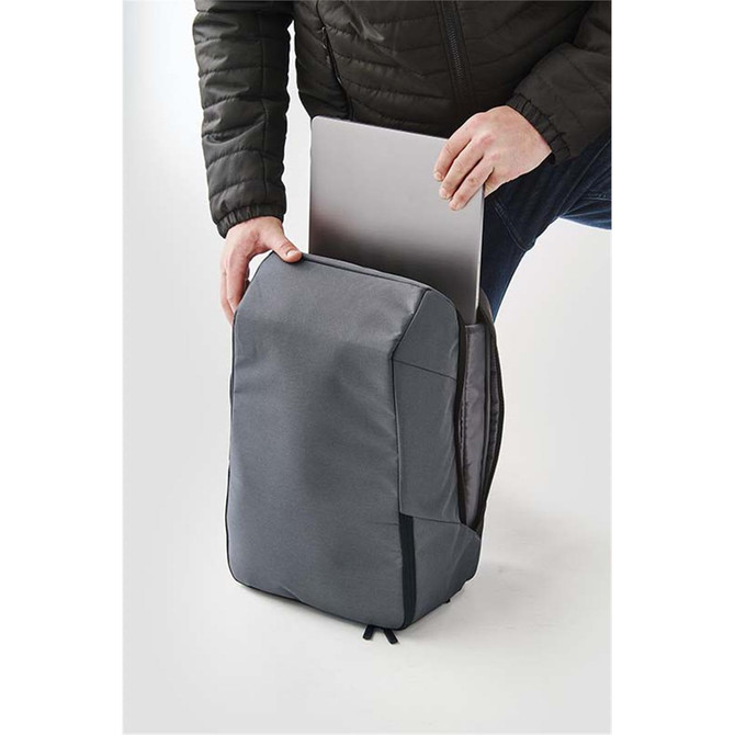 A grey backpack being used to store a laptop, with a person holding the bag open. It has a logo on the front.