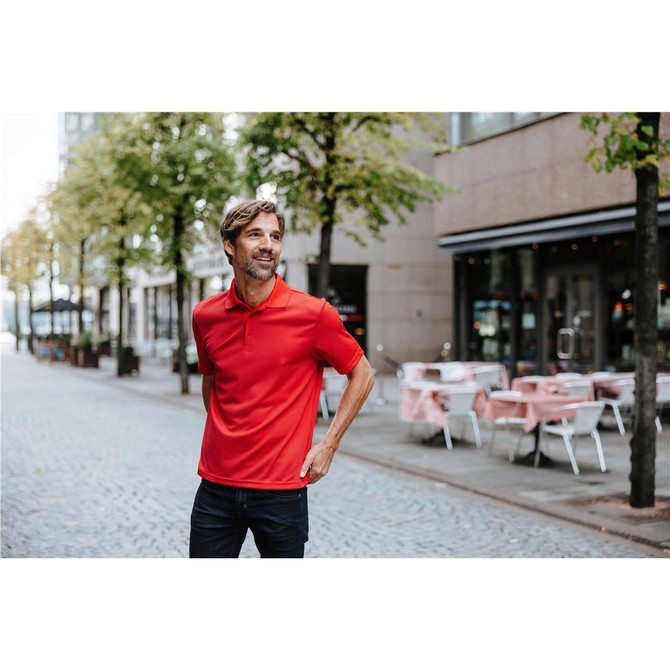 A man wearing a bright red polo shirt stands on a cobbled street with outdoor seating visible in the background.