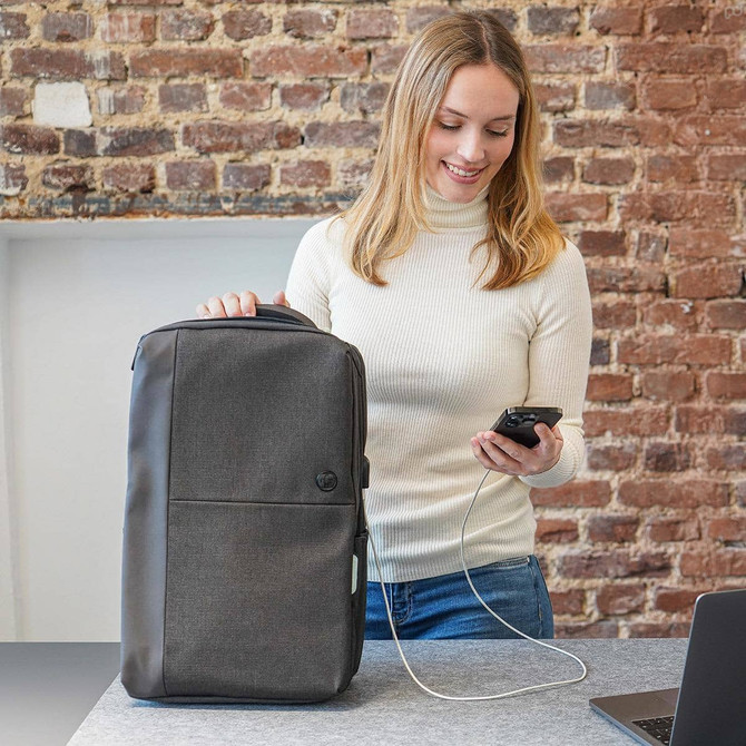 A grey Swissdigital Arosa Backpack with a logo, placed beside a laptop, while a person is using a smartphone.