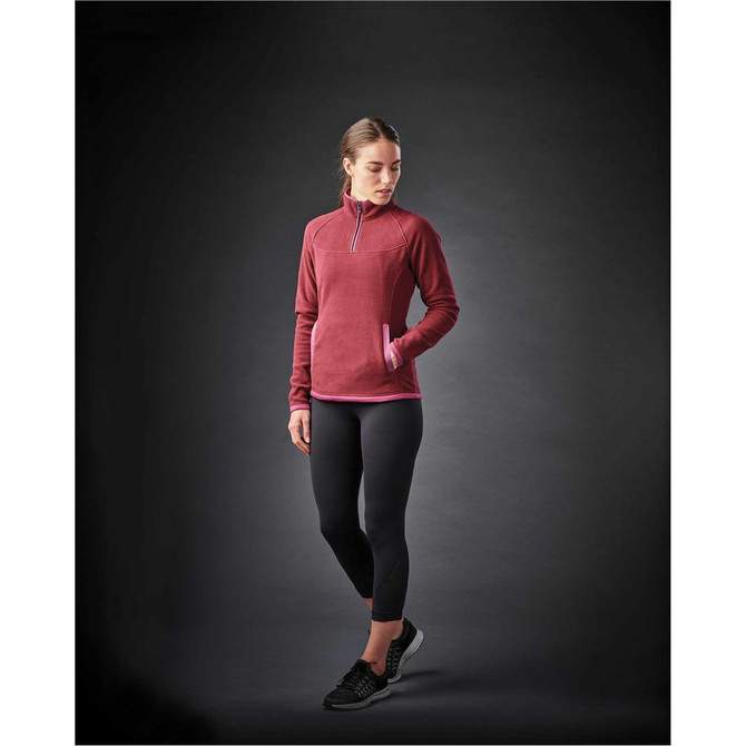 A model wearing a burgundy women's fleece jumper with a quarter zip, paired with black leggings and trainers.