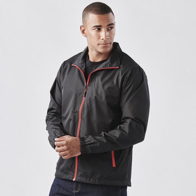 A man wearing a black jacket with red accents, featuring a zipped front and elastic cuffs. The jacket has a logo.