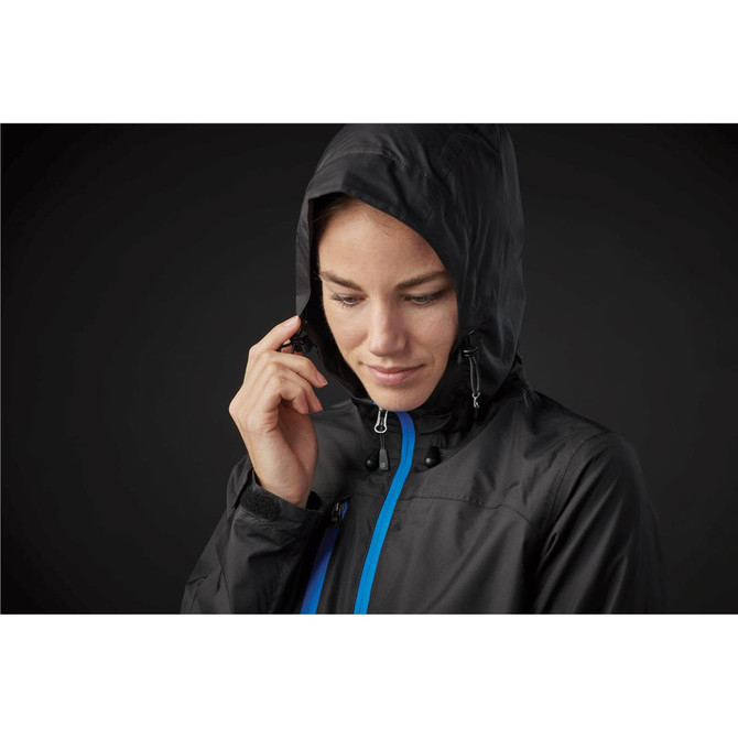 A woman wears a black rain jacket with a hood, featuring blue accents and a logo.
