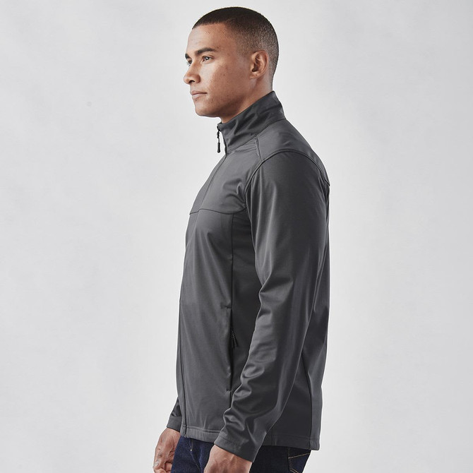 A man wearing a grey lightweight softshell jacket with a high collar and zippered pockets, featuring a logo.