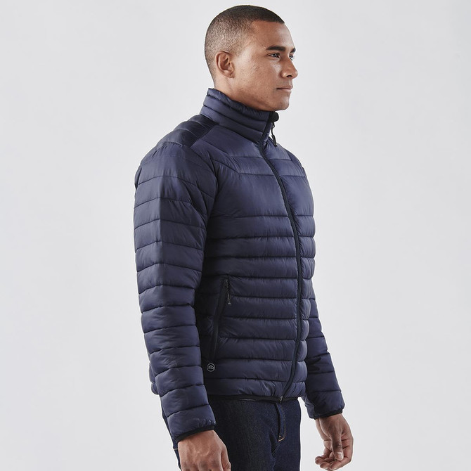 A navy blue puffer jacket featuring a zip front and a high collar, worn by a model. It has a logo on the side.