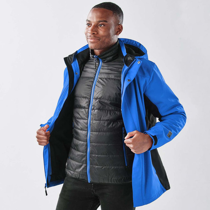 A man wearing a blue 3-in-1 jacket, layered with a black puffer inner, featuring a logo.