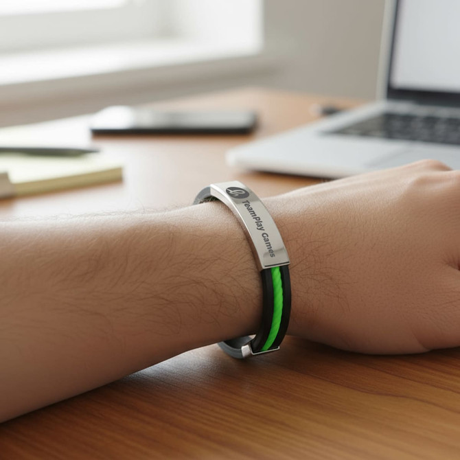 A sleek bracelet featuring a silver clasp and black and green silicone bands, resting on a wooden desk.