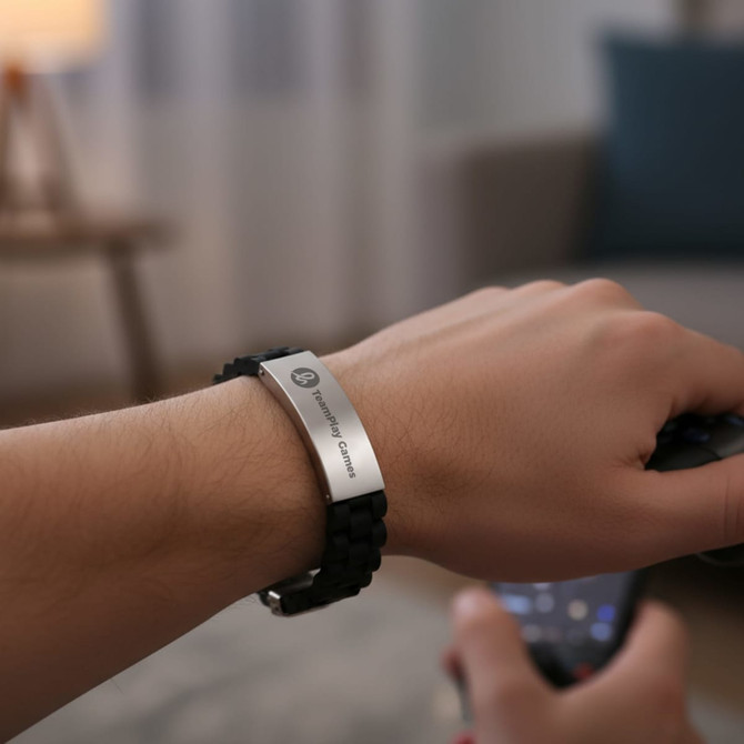 A hand wearing a black silica bracelet with a silver metal clasp. The background features a soft, homey interior.