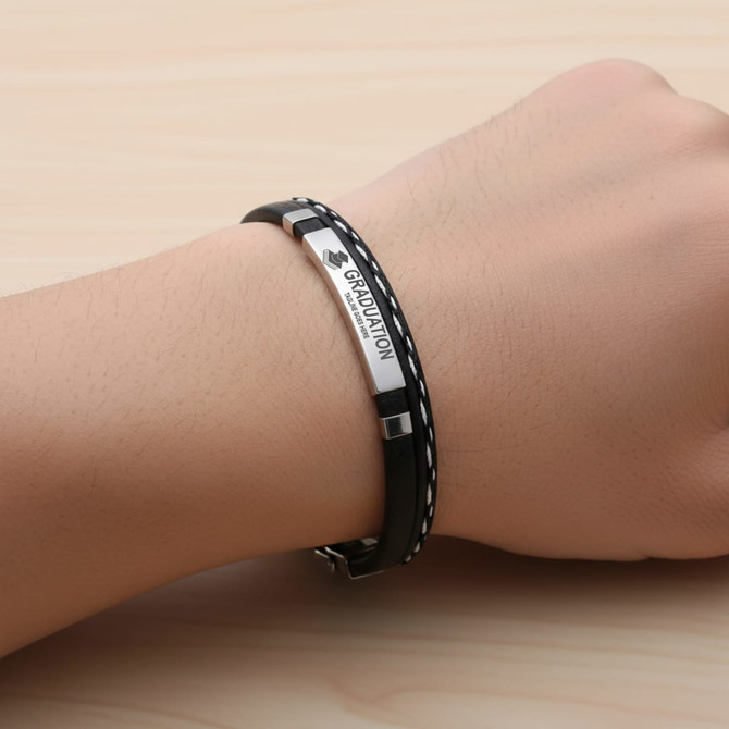 A black and silver personalised leather bracelet worn on a hand, featuring a logo and decorative stitching.