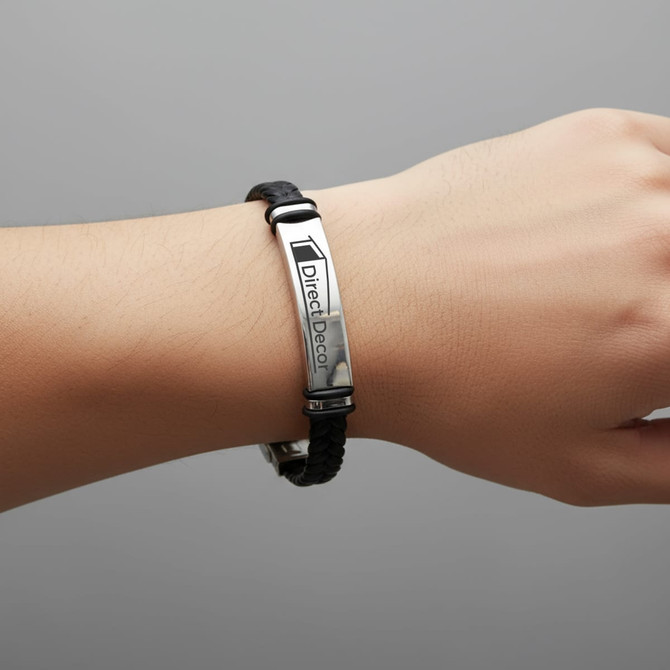 A black leather twine bracelet with a silver metal plate, featuring a logo. Worn on a person’s wrist.