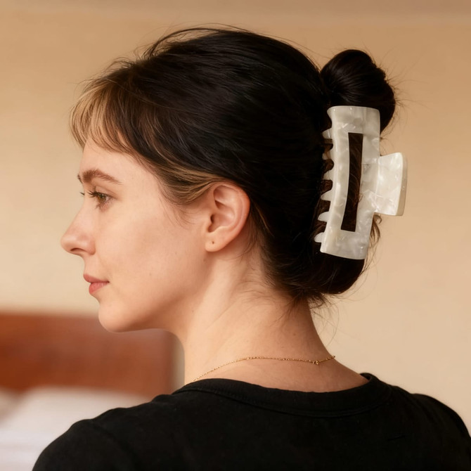 A hair claw clip in a marbled design, clasping a bun of dark hair. The clip features a logo.