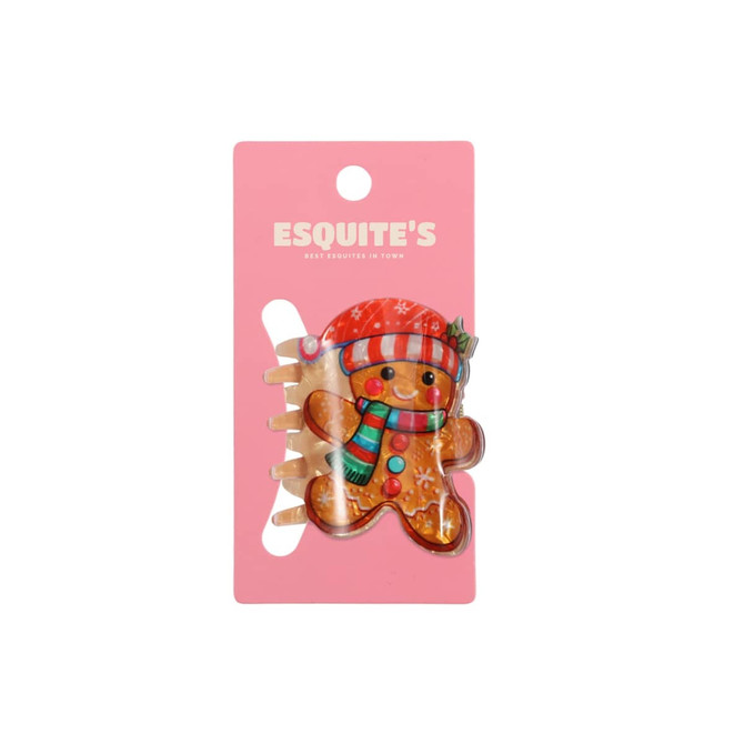 A gingerbread man hair claw in festive colours, featuring a red hat and scarf, on a pink backing with a logo.