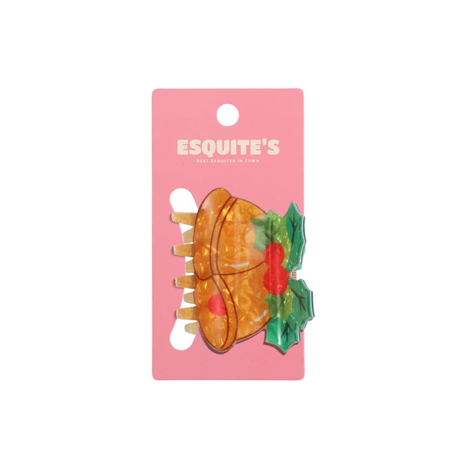 A Christmas-themed hair claw featuring a bell design in orange and green on a pink backing with branding.