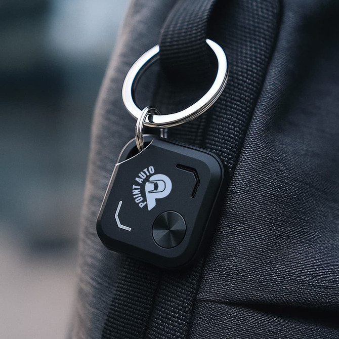 A black Bluetooth tracker attached to a bag, featuring a keyring and a logo.