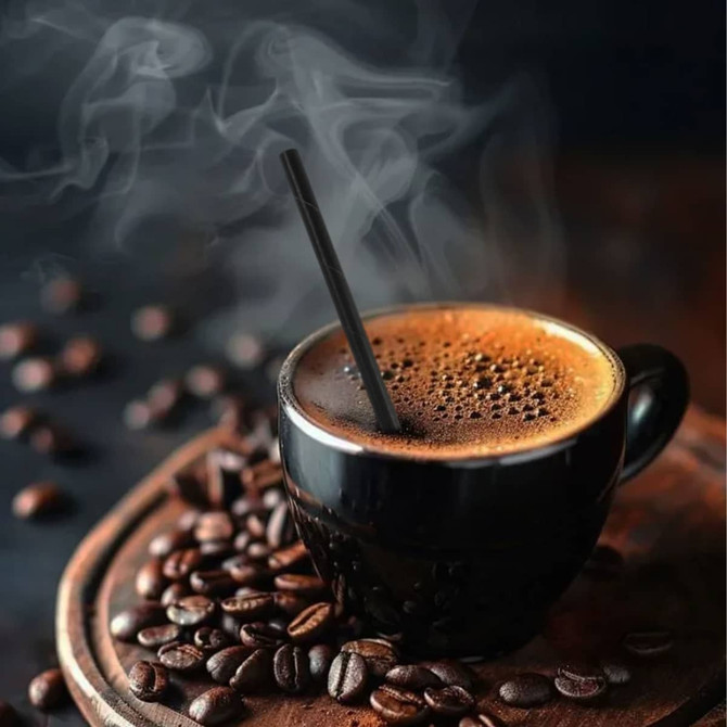 A black coffee cup filled with steaming coffee, featuring a black paper straw and surrounded by coffee beans.
