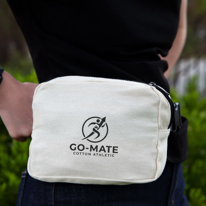 A beige cotton belt bag with a logo, worn on the waist against a green background.
