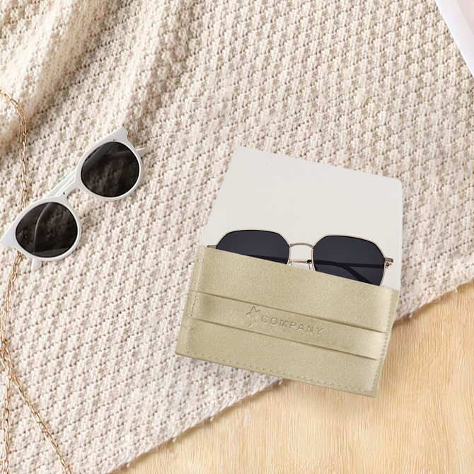 A PU leather glasses pouch in gold, holding a pair of dark sunglasses, set on a textured fabric background.