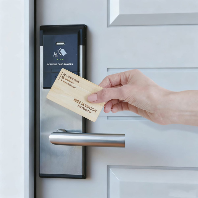 A bamboo business card is being held near a contactless door lock with a sleek silver handle.