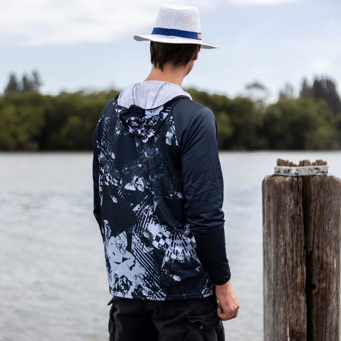A men's polyester sublimated 1/4 zip fishing hoodie in navy and grey, featuring a hood and a logo, worn by a person by the water.