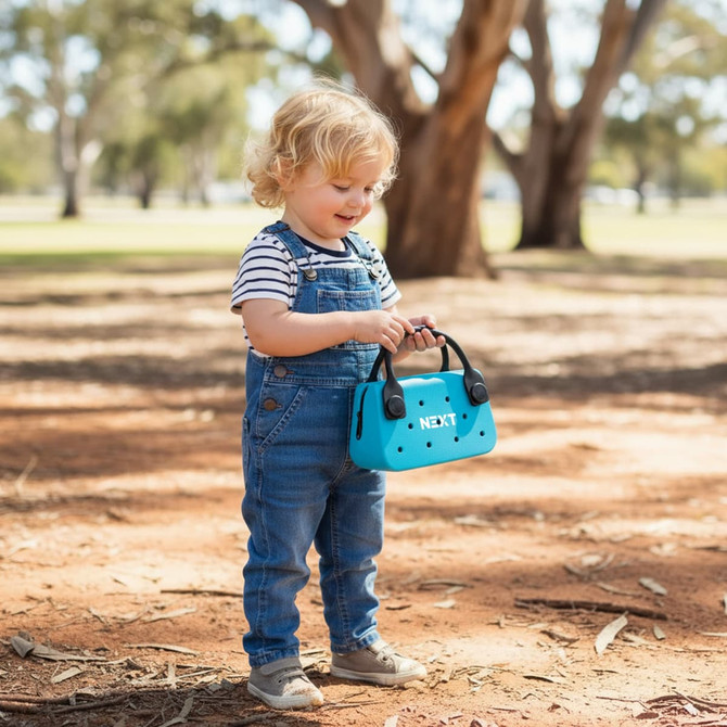 A child holds a bright blue EVA Holes Mini Handbag while standing on a dirt surface under trees.