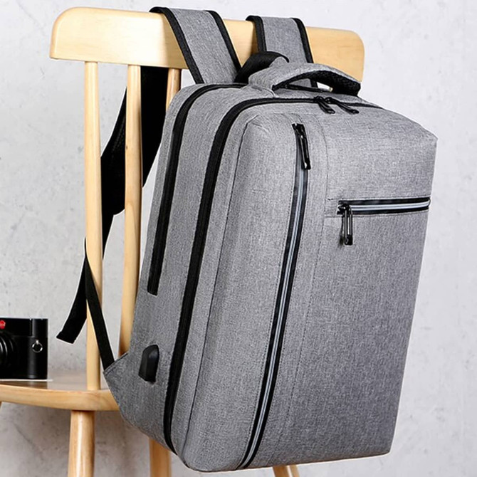 A sleek grey laptop backpack with multiple compartments hanging on a wooden chair. It features a logo on the side.