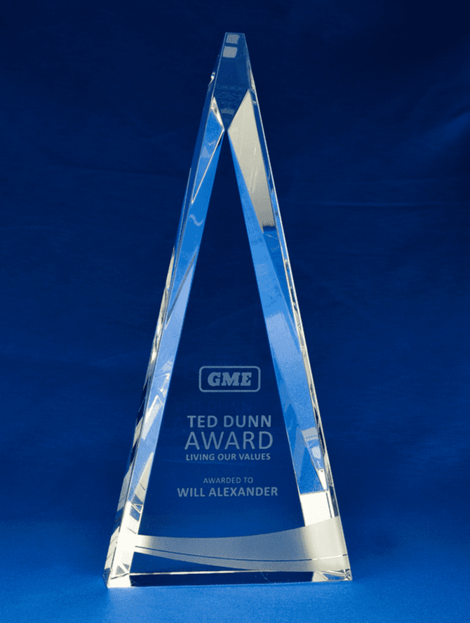A large, clear crystal triangular award with a branding logo, resting on a blue background.