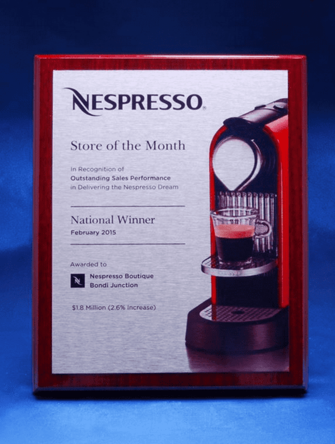 A printed award plaque on a piano finish timber base, featuring a Nespresso coffee machine. The plaque has a silver background.
