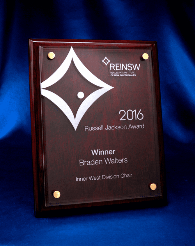 A rosewood plaque featuring a laser-engraved acrylic panel, displaying an award design. It has a glossy finish and gold accents.