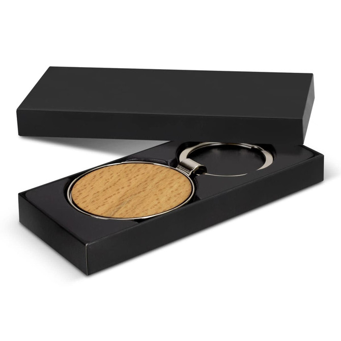 A round wooden key ring displayed in a black gift box, featuring a metal ring and a smooth, natural finish.