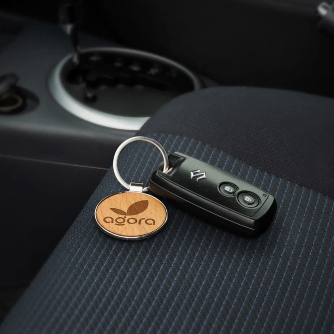 A round wooden key ring with a logo, resting beside a black car key on a patterned fabric seat.