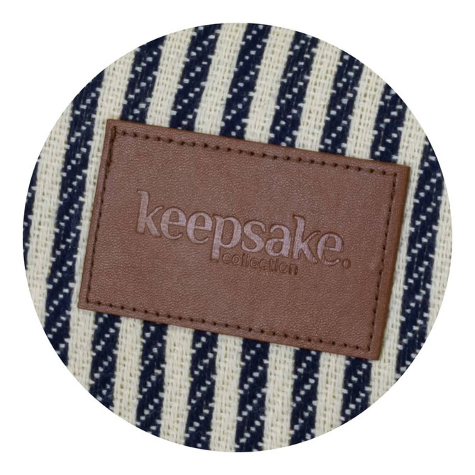 A striped picnic blanket features a brown leather tag with branding. The colours are cream and navy blue.