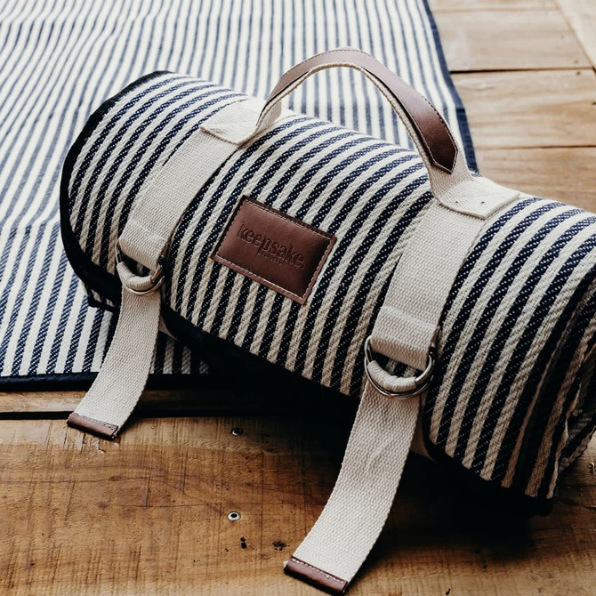 A rolled picnic blanket in navy and white stripes, with a leather handle and logo.