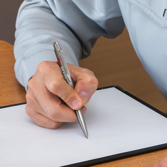 A metal pen with a silver finish held in a hand, writing on a blank sheet of paper. The pen features a logo.