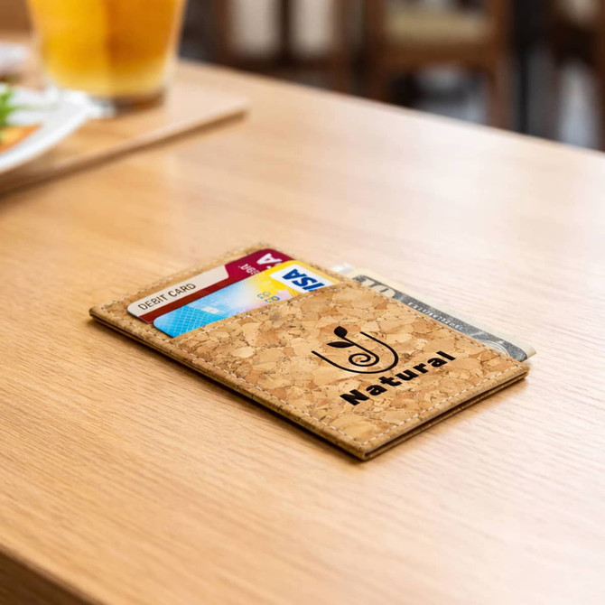 A cork card wallet in a natural shade, laying on a wooden table with visible credit cards inside.