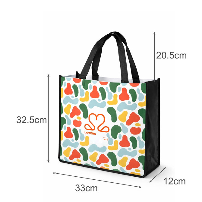 A vibrant tote bag featuring a multi-coloured abstract pattern, black handles, and a logo on one side.