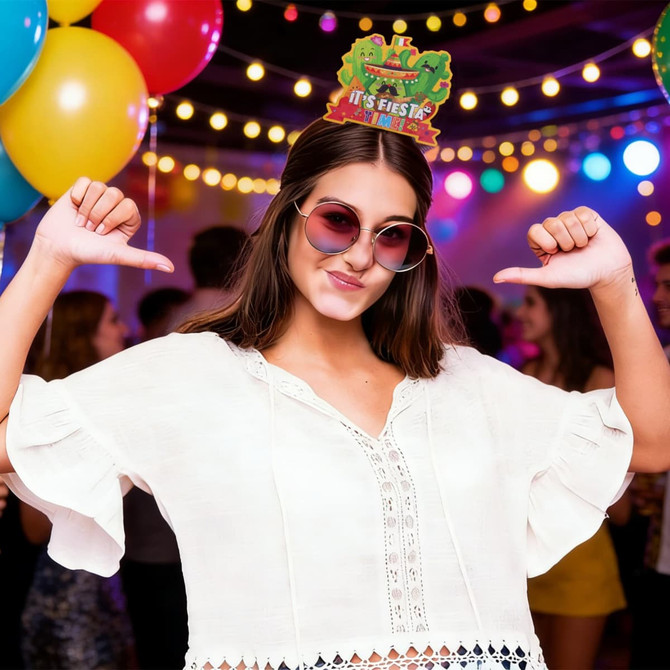 A woman wearing a white top and large sunglasses, with a festive headband, surrounded by colourful balloons and party lights.