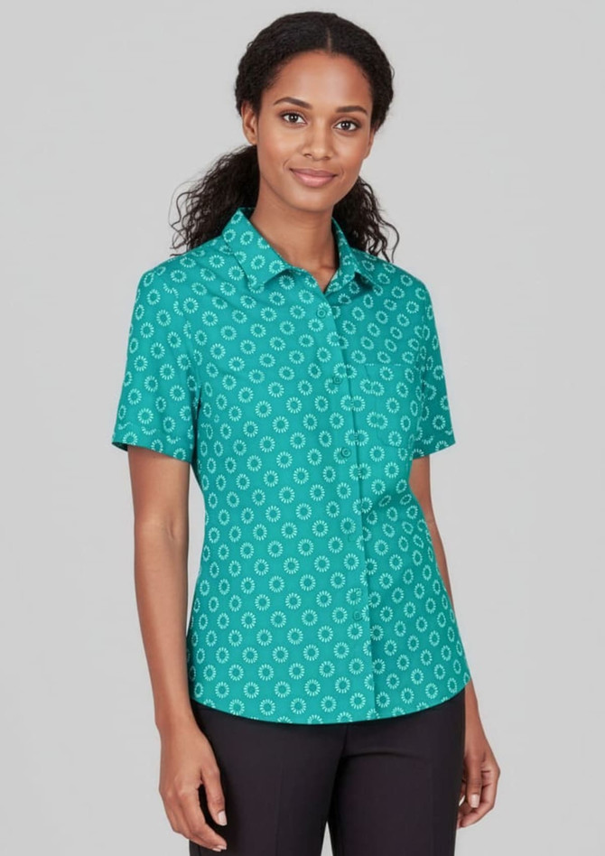 A short sleeve shirt in teal featuring a daisy print pattern and a button-up front. The model poses against a neutral background.