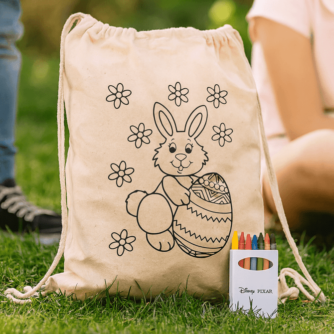 A cream drawstring bag featuring a bunny and floral design, accompanied by a crayon set in various colours.