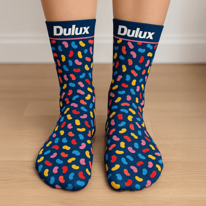 A pair of navy socks decorated with colourful bean-shaped patterns, featuring a logo at the top.