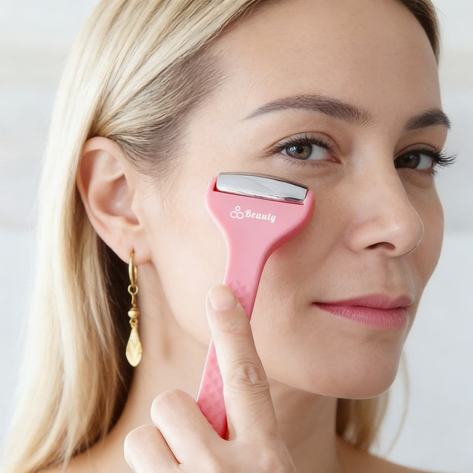 A pink double-headed ice massager roller held near a woman's face, featuring a logo on the handle.