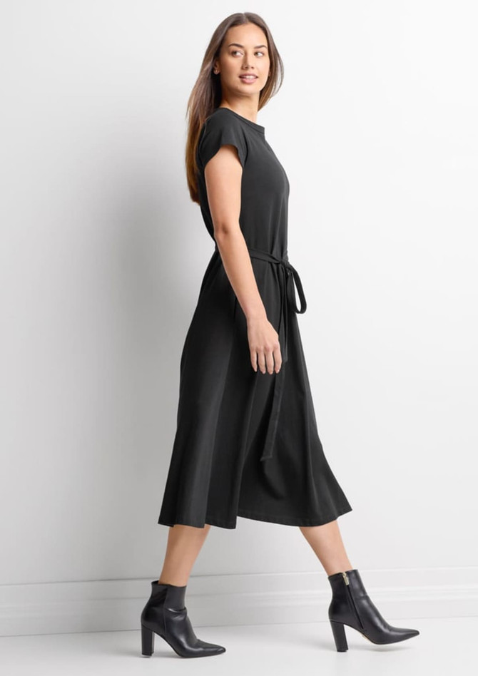 A black midi dress with short sleeves and a waist tie, paired with stylish ankle boots. It features a subtle logo.